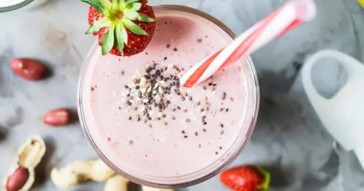 Vitamix Peanut Butter And Jelly smoothie in a glass, on my kitchen counter, surrounded by fresh fruit and vegetables.