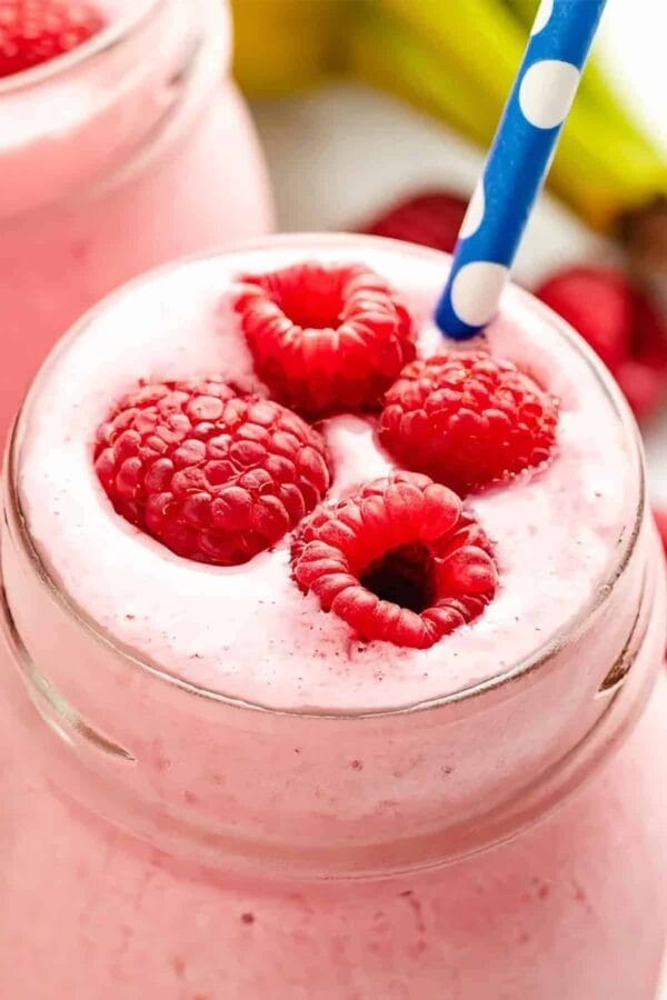 Vitamix Peanut Butter Berry smoothie in a glass, on my kitchen counter, surrounded by fresh fruit and vegetables.