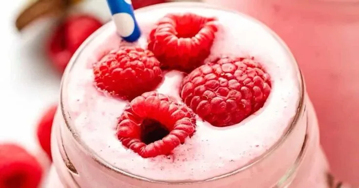 Vitamix Peanut Butter Berry smoothie in a glass, on my kitchen counter, surrounded by fresh fruit and vegetables.