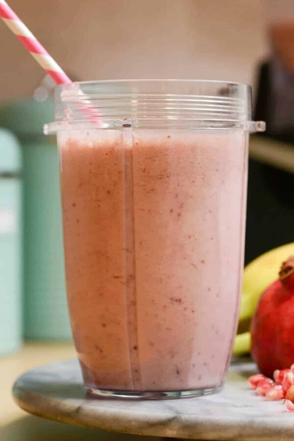 Vitamix Pomegranate Boost smoothie in a glass, on my kitchen counter, surrounded by fresh fruit and vegetables.