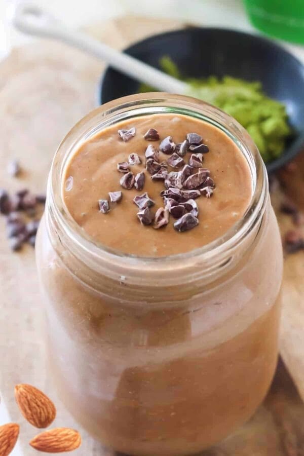 Chocolate Matcha smoothie in a glass, on my kitchen counter, surrounded by chocolate curls and green tea matcha powder.