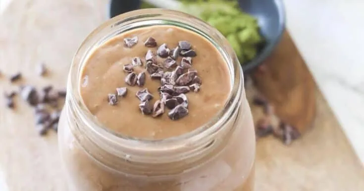 Chocolate Matcha smoothie in a glass, on my kitchen counter, surrounded by chocolate curls and green tea matcha powder.