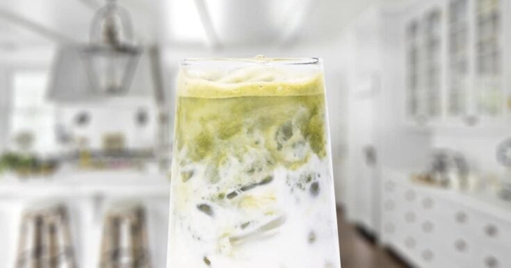 Classic Matcha smoothie in a glass, on my kitchen counter, surrounded by fresh fruit and green tea matcha powder.