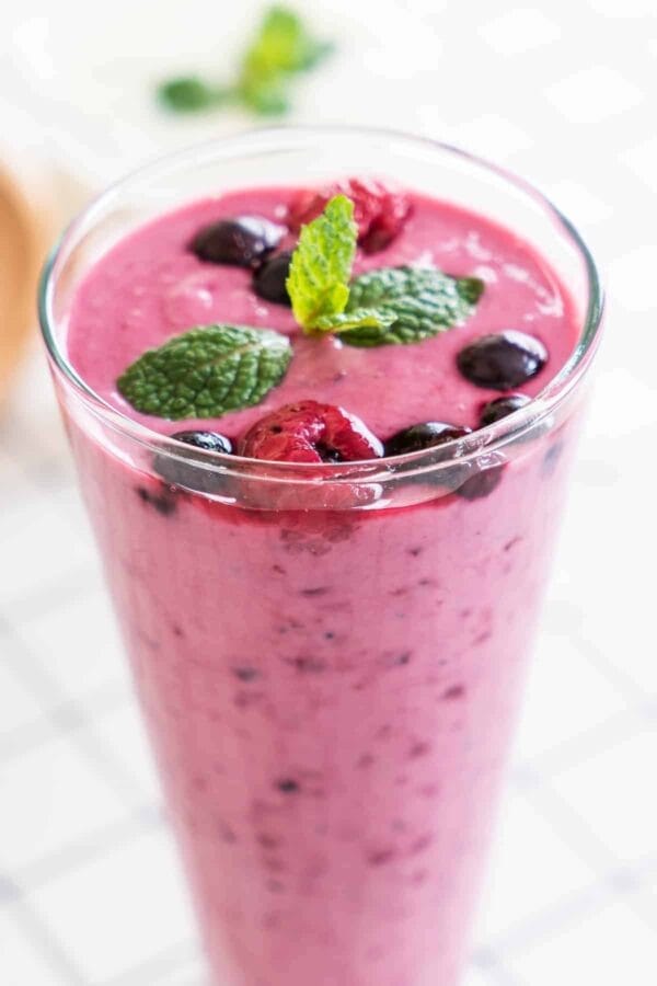 Ninja Blender Berry Good Day smoothie in a glass, on my kitchen counter, surrounded by fresh fruit.
