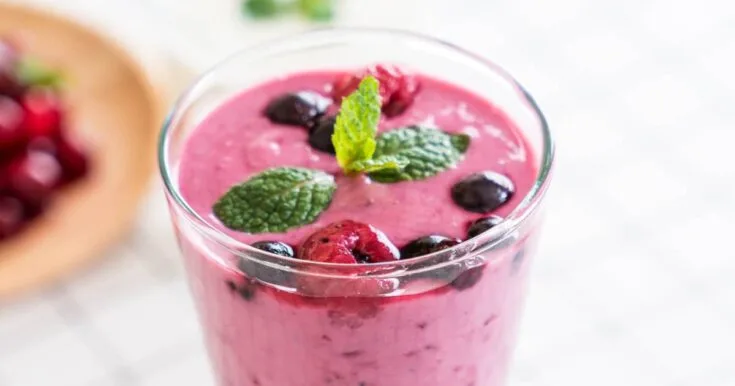 Ninja Blender Berry Good Day smoothie in a glass, on my kitchen counter, surrounded by fresh fruit.