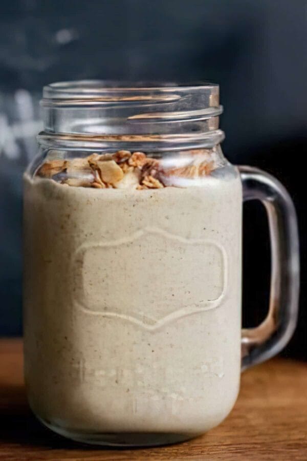 Ninja Blender Choco Nut Butter Protein smoothie in a glass, on my kitchen counter, surrounded by chocolate and nuts.