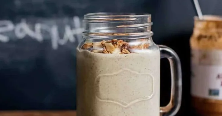 Ninja Blender Choco Nut Butter Protein smoothie in a glass, on my kitchen counter, surrounded by chocolate and nuts.