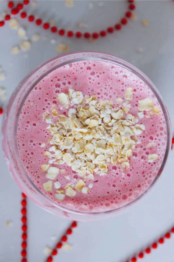 Ninja Blender Cranberry Oat smoothie in a glass, on my kitchen counter, surrounded by rolled oats.