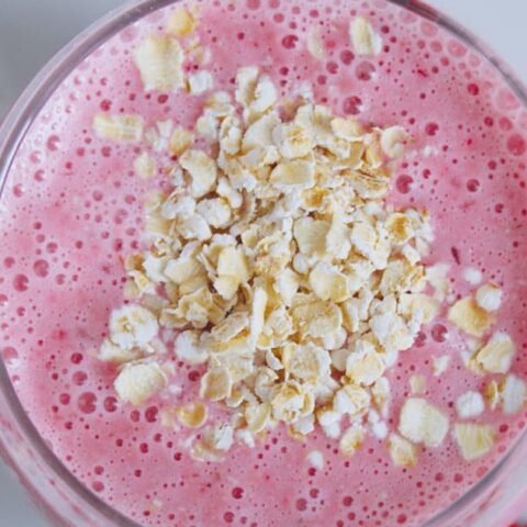Ninja Blender Cranberry Oat smoothie in a glass, on my kitchen counter, surrounded by rolled oats.