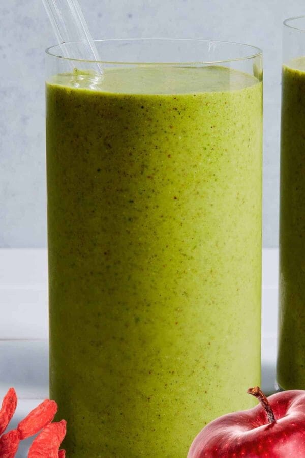Ninja Blender Dandy Green Machine smoothie in a glass, on my kitchen counter, surrounded by fresh fruit and vegetables.