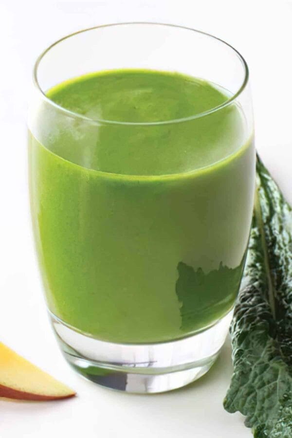 Ninja Blender Lean Green smoothie in a glass, on my kitchen counter, surrounded by fresh fruit and vegetables.