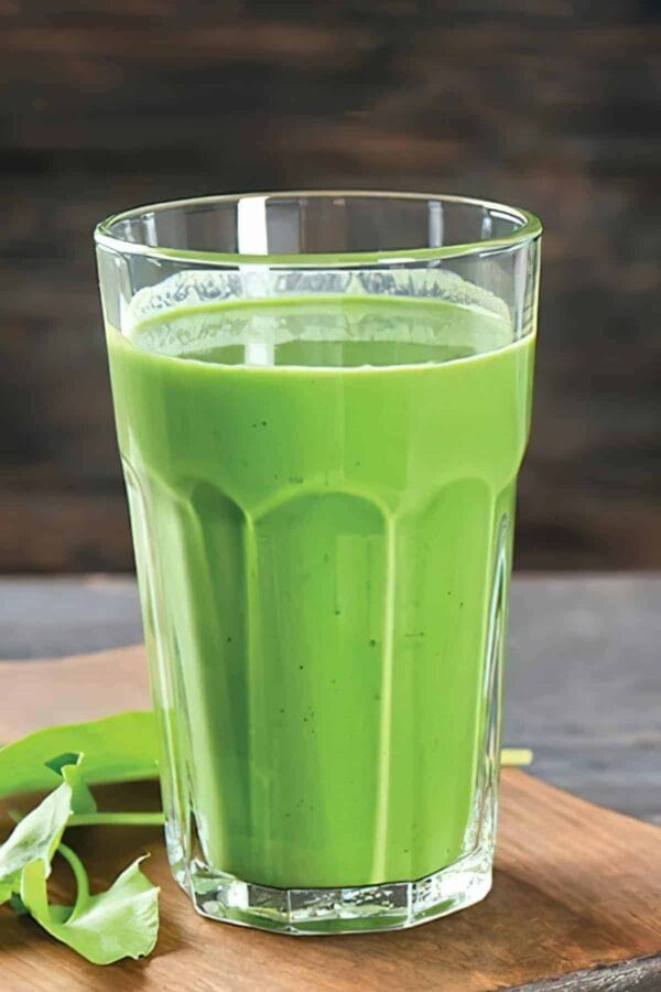 Ninja Blender Pineapple Apple Mint smoothie in a glass, on my kitchen counter, surrounded by fresh fruit and vegetables.