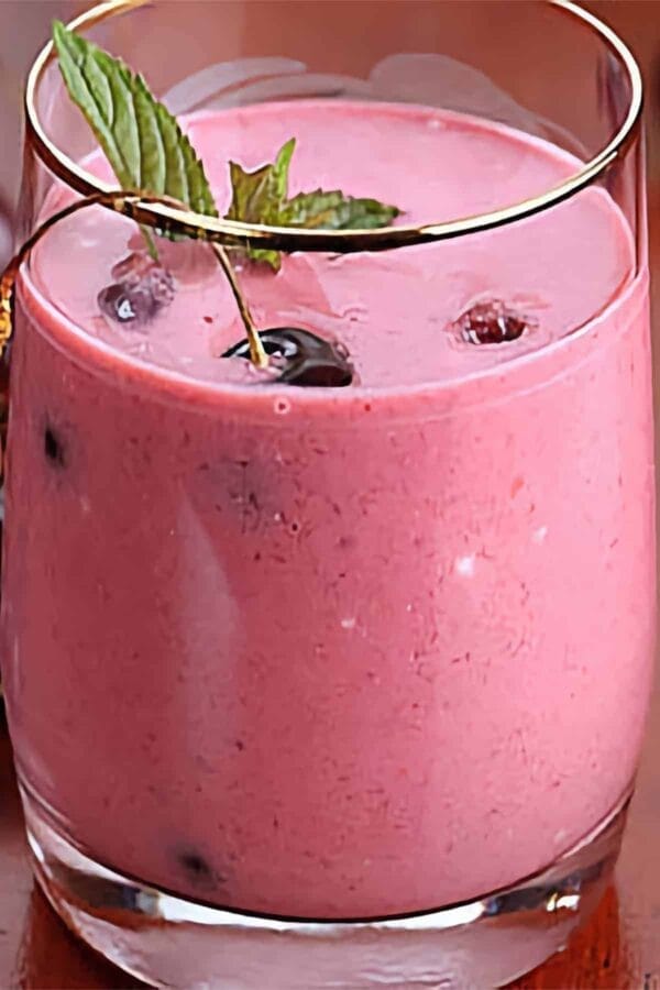 Ninja Blender Sweet Cherry smoothie in a glass, on my kitchen counter, surrounded by fresh fruit.