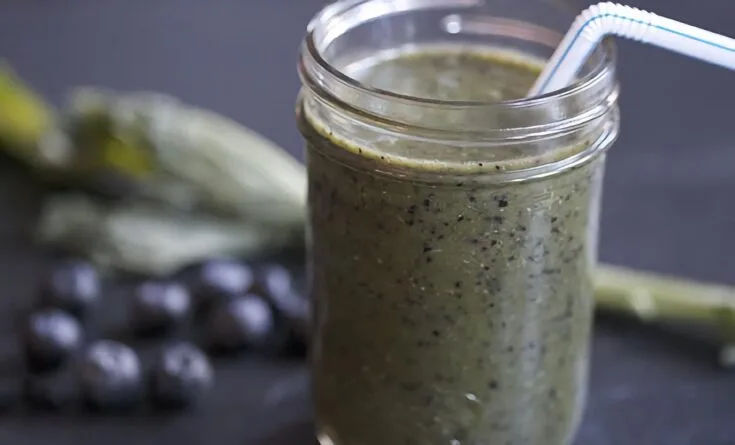 Flat Belly Weight Loss smoothie in a glass, on my kitchen counter, surrounded by fresh fruit and vegetables.