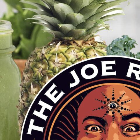 Joe Rogan Kale Shake smoothie in a glass, on my kitchen counter, surrounded by fresh fruit, vegetables, and a Joe Rogan Podcast sticker.