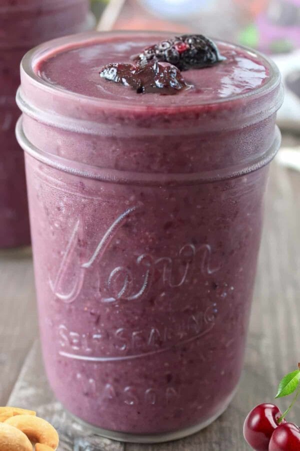 NutriBullet Blackberry Cherry Cashew smoothie in a glass, on my kitchen counter, surrounded by fresh fruit and nuts.