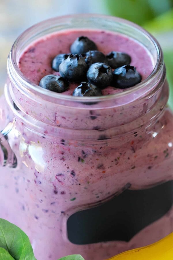 NutriBullet Blueberry Forever smoothie in a glass, on my kitchen counter, surrounded by fresh fruit and vegetables.