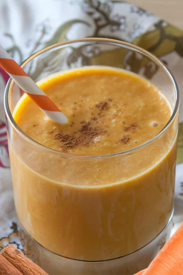 NutriBullet Carrot Cake smoothie in a glass, on my kitchen counter, surrounded by fresh vegetables and cinnamon.