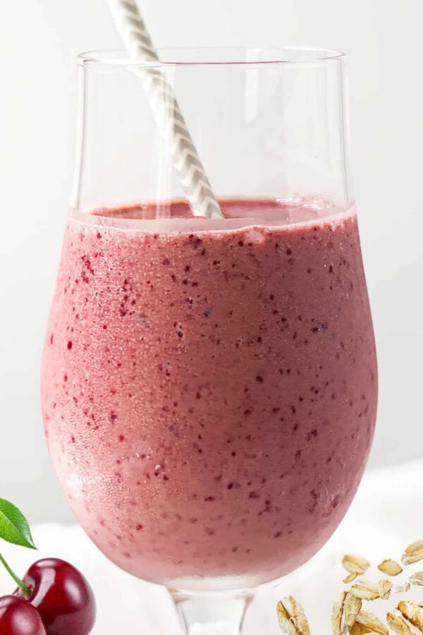 NutriBullet Cherry And Oats Bedtime smoothie in a glass, on my kitchen counter, surrounded by fresh fruit and rolled oats.