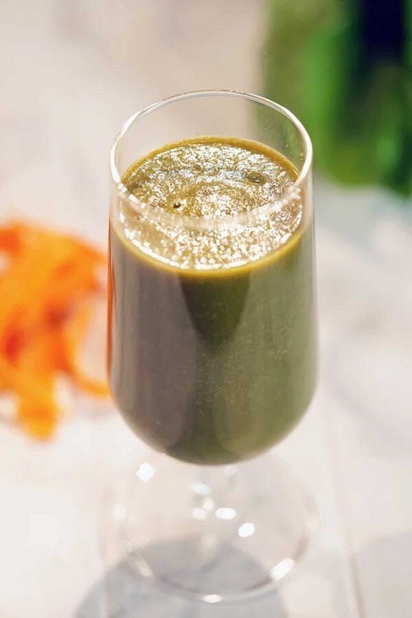 Paleo Diet smoothie in a glass, on my kitchen counter, surrounded by fresh vegetables.