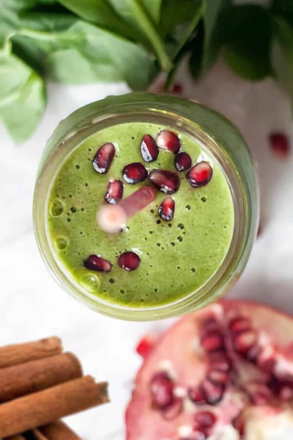 NutriBullet Green Pomegranate Blast smoothie in a glass, on my kitchen counter, surrounded by fresh fruit and cinnamon.