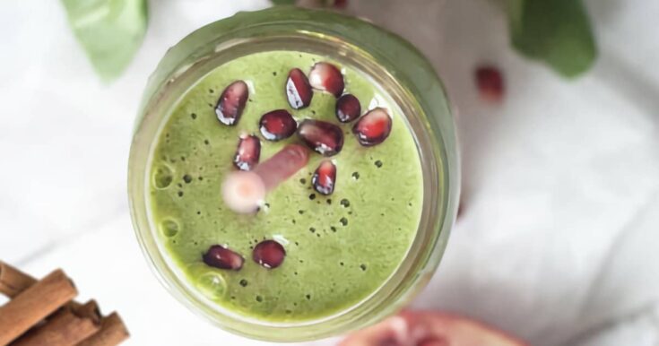 NutriBullet Green Pomegranate Blast smoothie in a glass, on my kitchen counter, surrounded by fresh fruit and cinnamon.