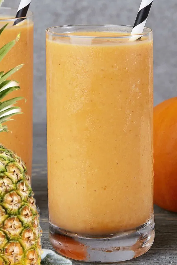 NutriBullet Pumpkin Pie Protein smoothie in a glass, on my kitchen counter, surrounded by fresh fruit and vegetables.