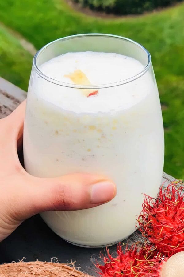 NutriBullet Rambutan Refresher smoothie in a glass, on my kitchen counter, surrounded by fresh fruit and coconut.