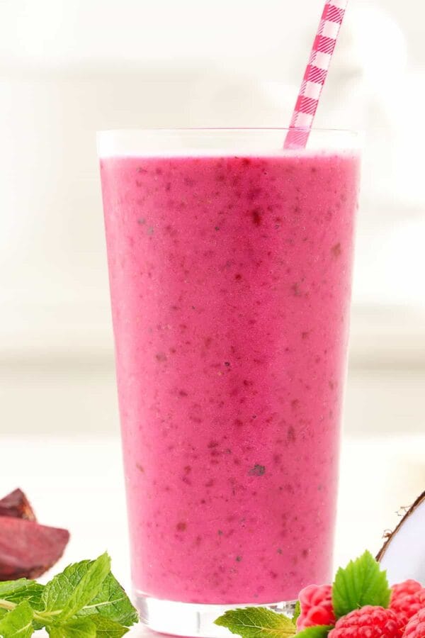 NutriBullet Raspberry Beet smoothie in a glass, on my kitchen counter, surrounded by fresh fruit and vegetables.