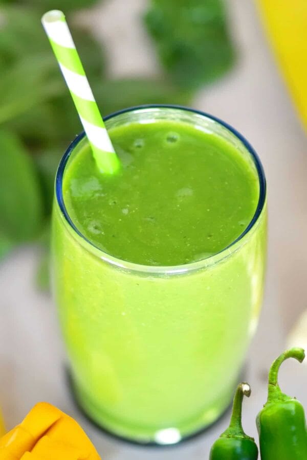 NutriBullet Spicy Mango Magic smoothie in a glass, on my kitchen counter, surrounded by fresh fruit and jalapenos.
