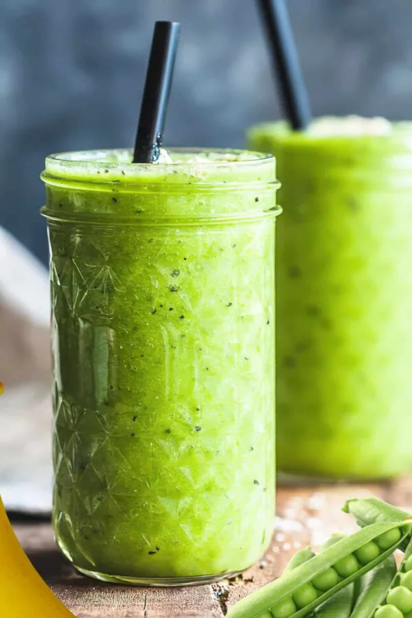 NutriBullet Spring Pea smoothie in a glass, on my kitchen counter, surrounded by fresh fruit and vegetables.