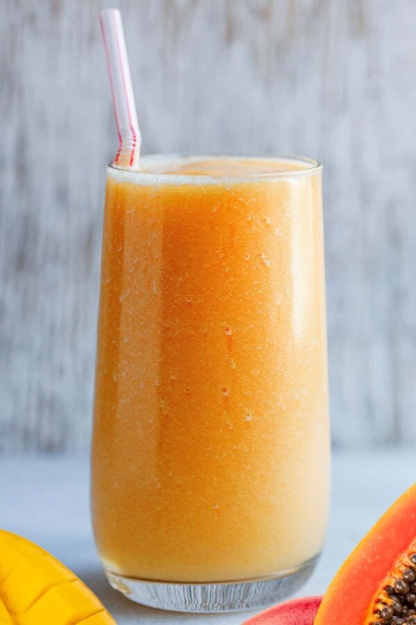 NutriBullet Tropical Candy Corn smoothie in a glass, on my kitchen counter, surrounded by fresh fruit.