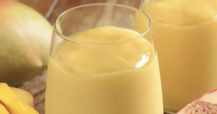 NutriBullet Zingy Orange Peach Mango smoothie in a glass, on my kitchen counter, surrounded by fresh fruit.