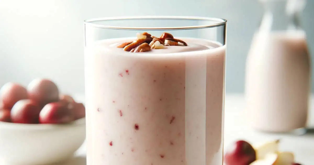 BlendJet Cran Apple Pecan smoothie in a glass, on my kitchen counter, surrounded by fresh fruit and nuts.