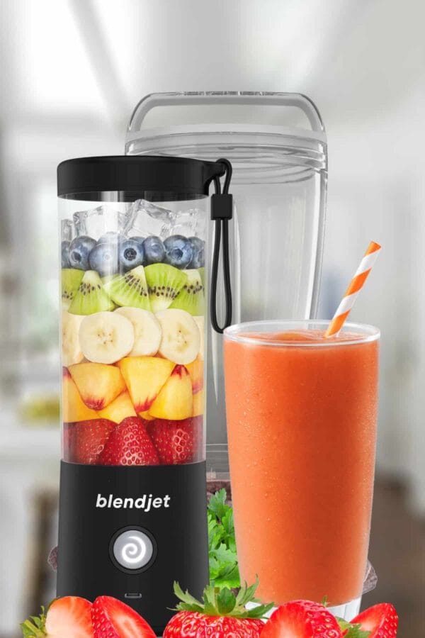 BlendJet blender next to a BlendJet smoothie in a glass, on my kitchen counter, surrounded by fresh fruit and vegetables.