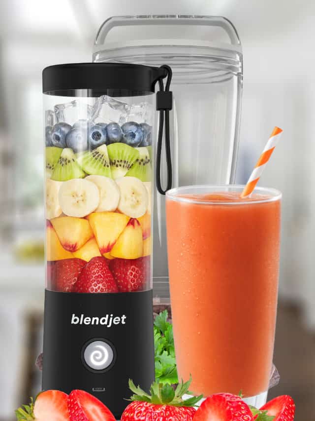 BlendJet blender next to a BlendJet smoothie in a glass, on my kitchen counter, surrounded by fresh fruit and vegetables.