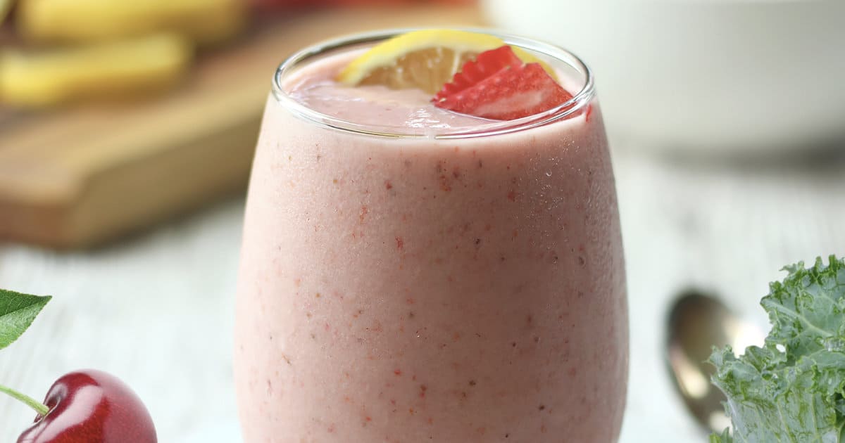 NutriBullet Pink Drink smoothie in a glass, on my kitchen counter, surrounded by fresh fruit.
