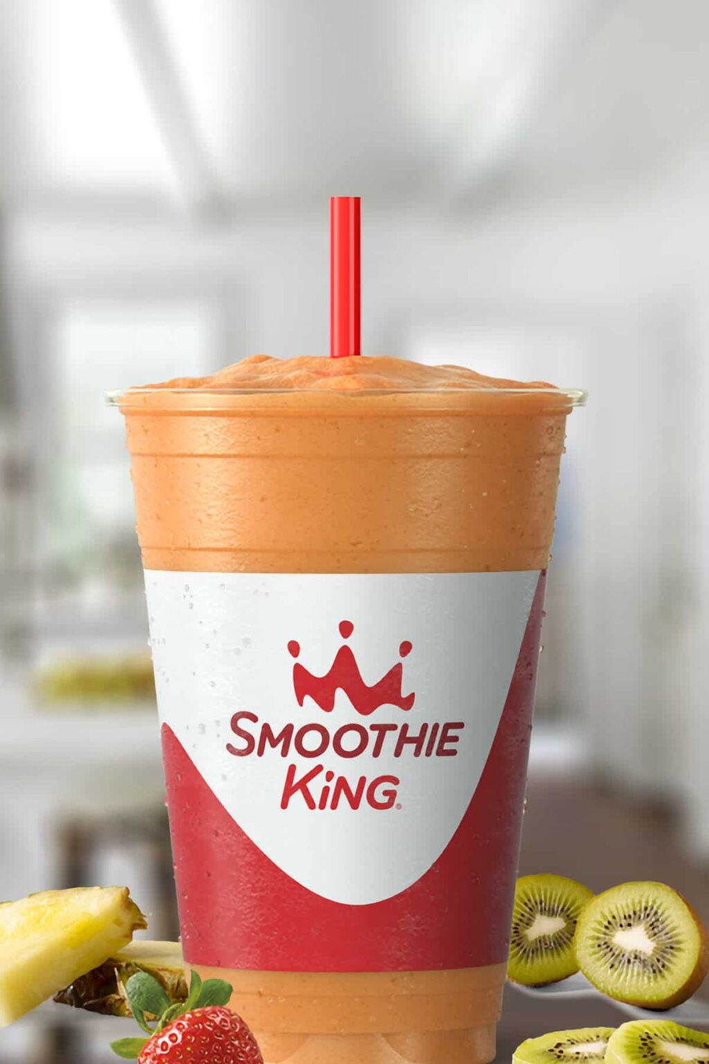 Smoothie King Pineapple Surf smoothie in a glass, on my kitchen counter, surrounded by fresh fruit.