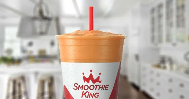 Smoothie King Pineapple Surf smoothie in a glass, on my kitchen counter, surrounded by fresh fruit.