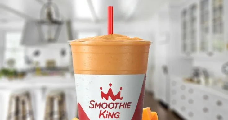 Smoothie King Pumpkin D-Lite smoothie in a glass, on my kitchen counter, surrounded by fresh fruit.