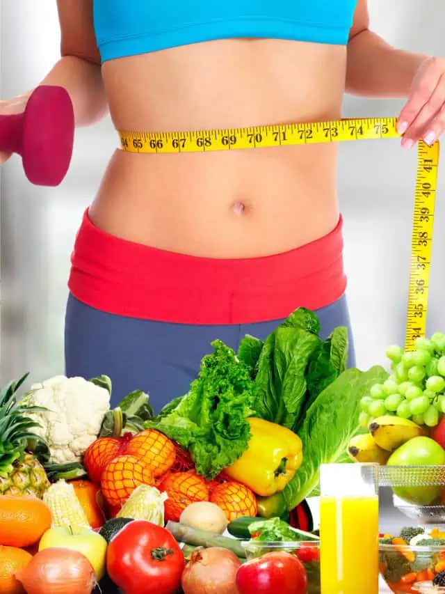 Fit woman with a flat belly, standing next to a weight loss smoothie, surrounded by fresh fruit and vegetables.