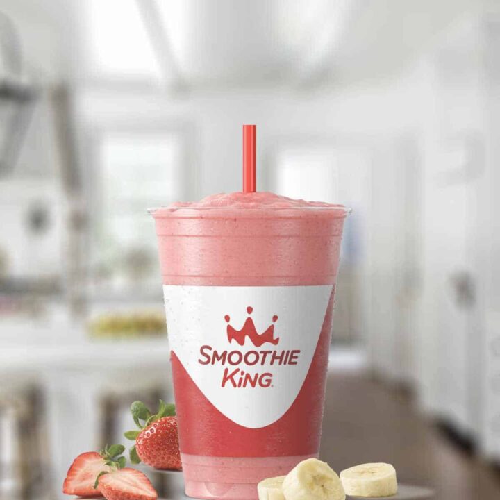 Smoothie King Angel Food smoothie in a glass, on my kitchen counter, surrounded by fresh fruit and vanilla.