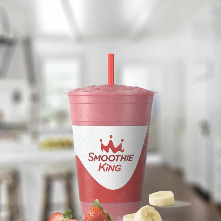 Smoothie King Banana Berry Treat smoothie in a glass, on my kitchen counter, surrounded by fresh fruit.