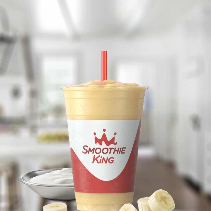Smoothie King Banana Boat smoothie in a glass, on my kitchen counter, surrounded by fresh fruit.
