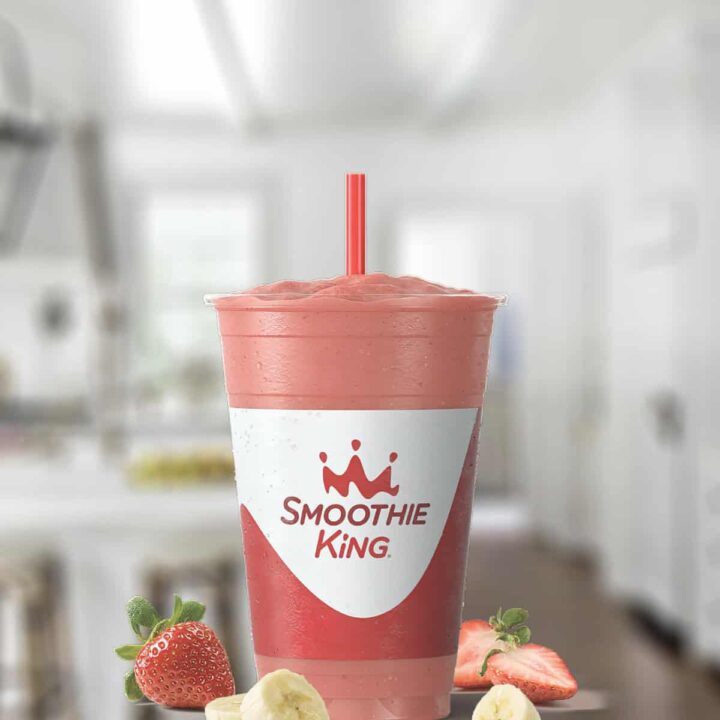 Smoothie King Caribbean Way smoothie in a glass, on my kitchen counter, surrounded by fresh fruit.