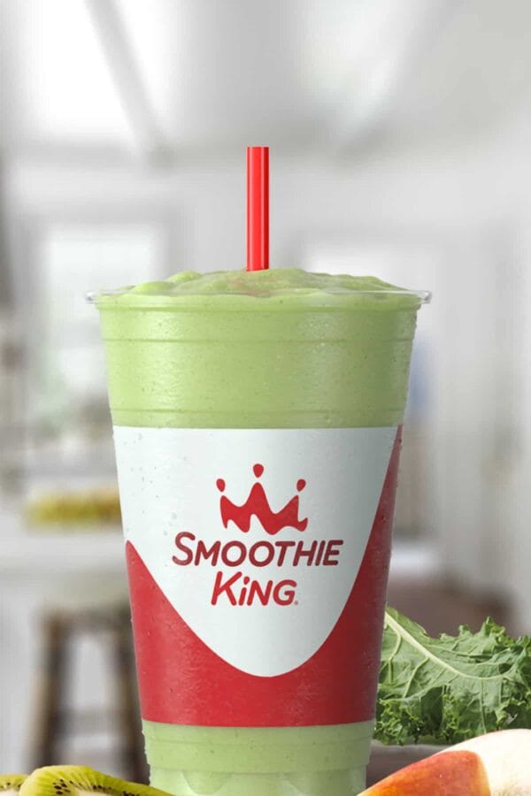 Smoothie King Kids Apple Kiwi Bunga smoothie in a glass, on my kitchen counter, surrounded by fresh fruit and vegetables.