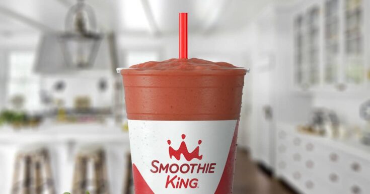 Smoothie King Kids CW Jr smoothie in a glass, on my kitchen counter, surrounded by fresh strawberries and bananas.