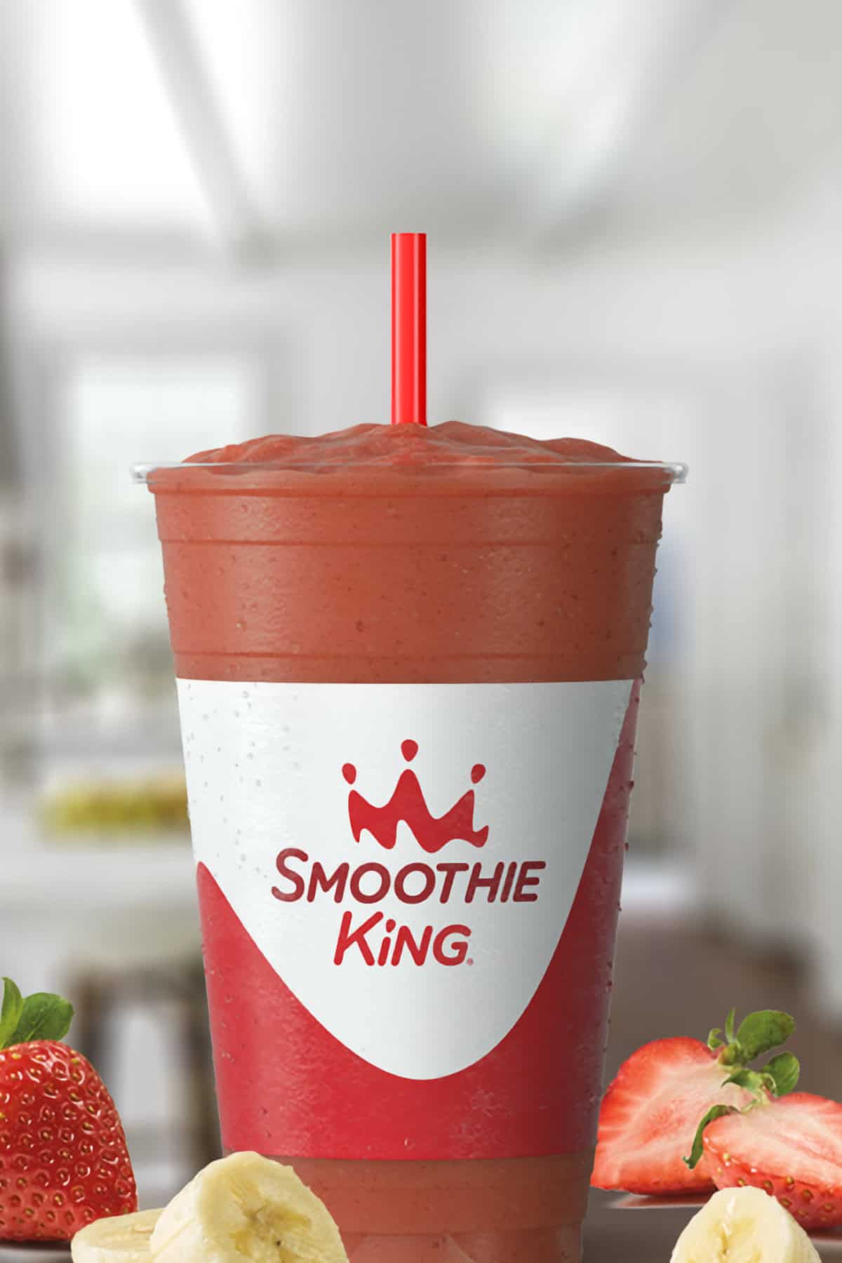 Smoothie King Kids CW Jr smoothie in a glass, on my kitchen counter, surrounded by fresh strawberries and bananas.