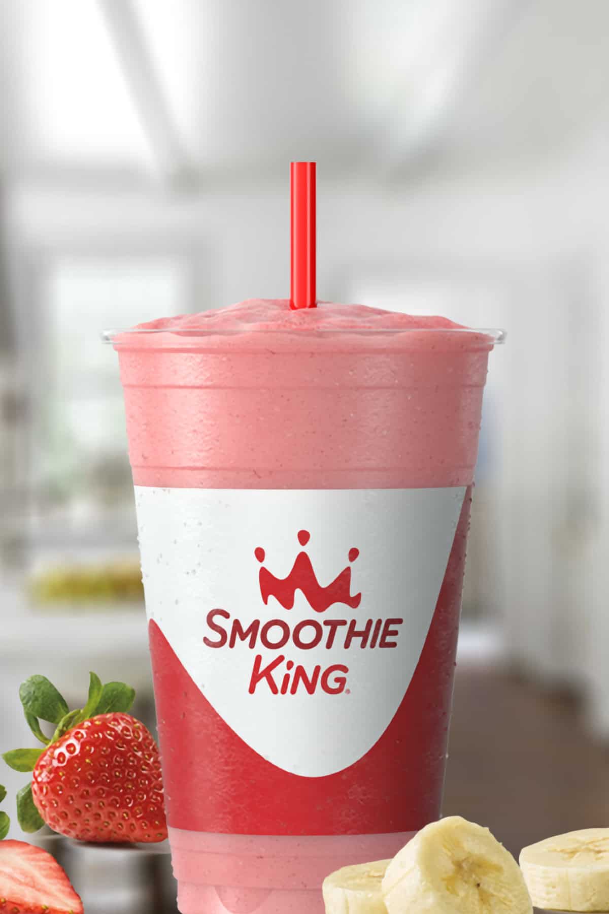 Smoothie King Kids Lil Angel smoothie in a glass, on my kitchen counter, surrounded by fresh strawberries and bananas.