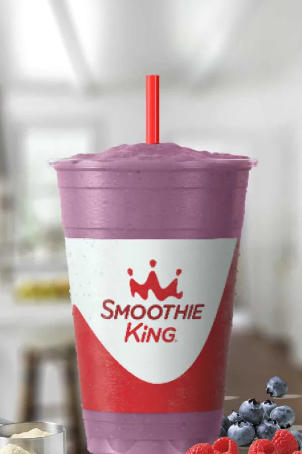 Smoothie King Power Meal Blueberry Raspberry smoothie in a glass, on my kitchen counter, surrounded by fresh blueberries and raspberries.